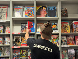 A Dragonsteel employee in a deerstalker cap reaches for a Spider-Man comic book on a shelf of other comics.